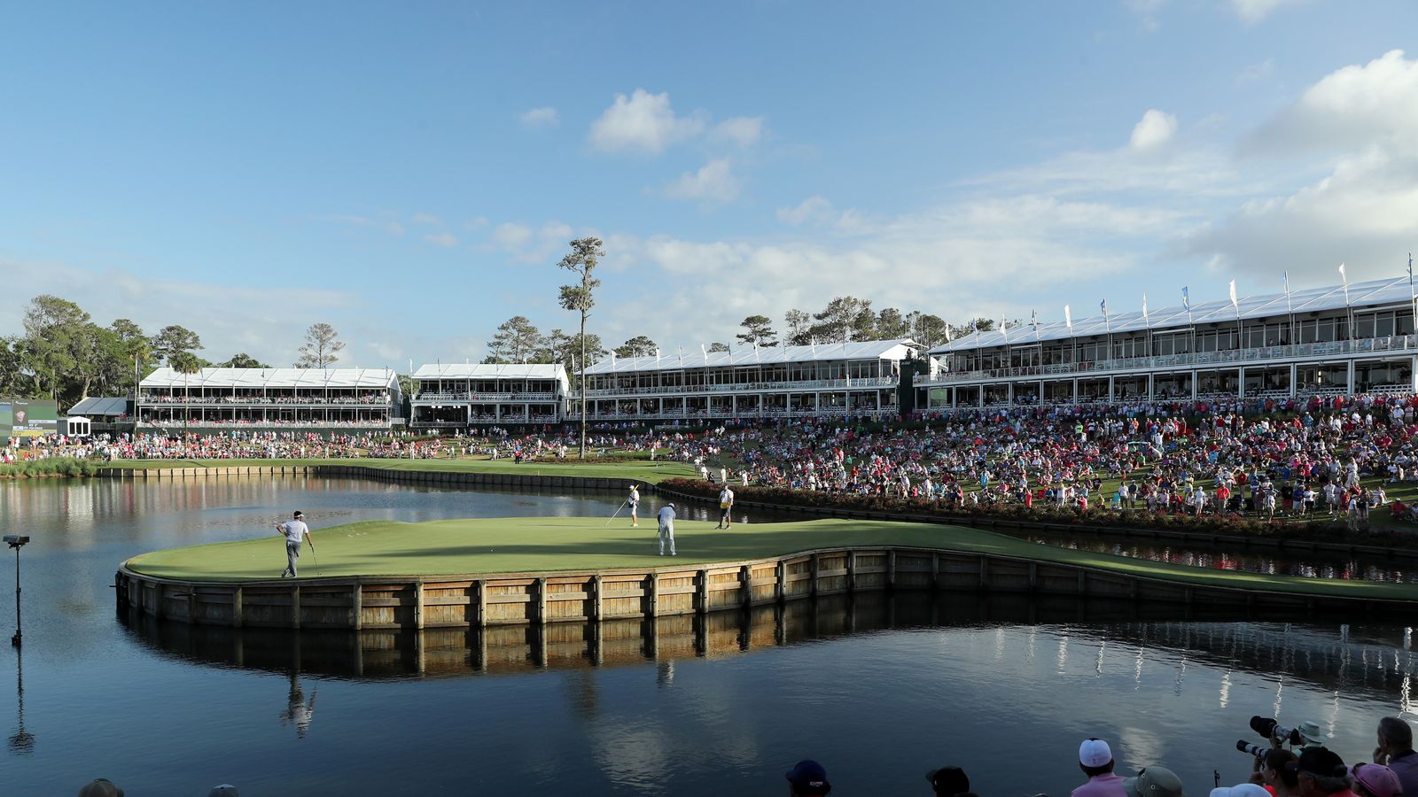 Golfers on the island green surrounded by crowds and grandstands at a major tournament